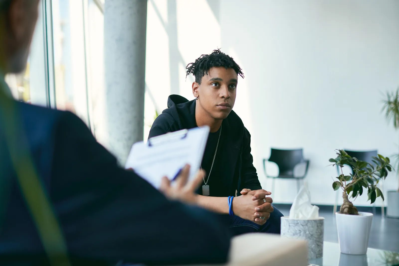 Teenager sitting for a counseling-style interview, hands clasped, listening to questions