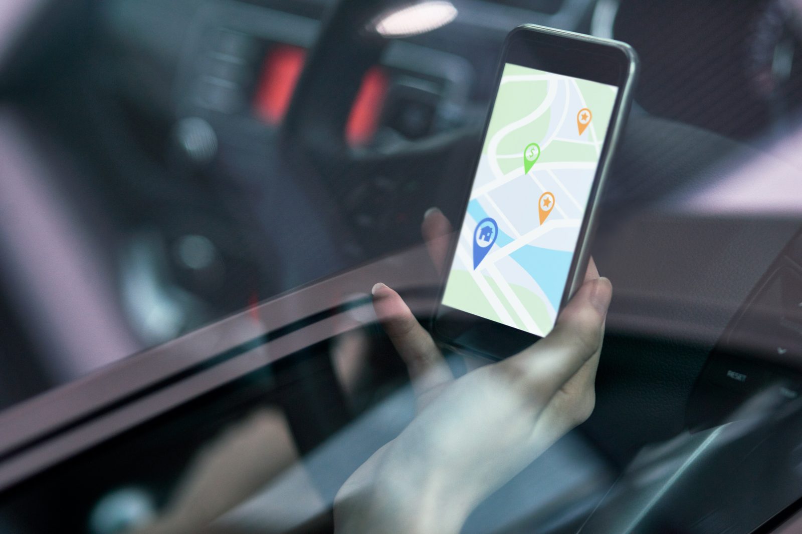 Hand holding a smartphone showing a map with location pins inside a car