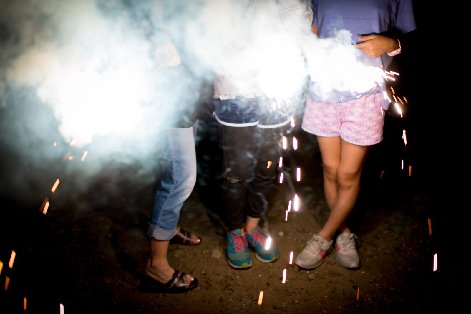 Teens holding lit sparklers in smoke at night